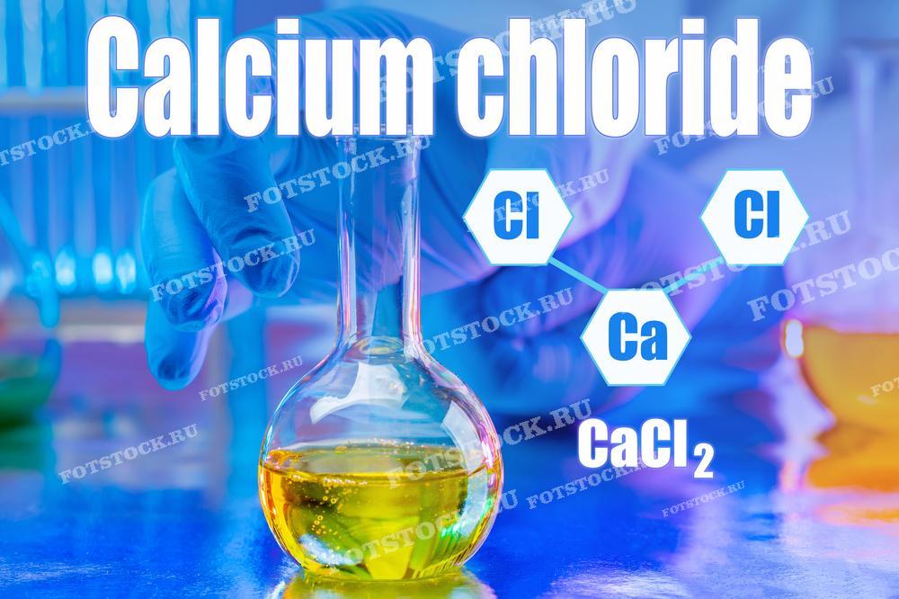 На фотографии изображены надпись "Calcium chloride", химическая формула CaCl2 и структурная формула соединения на синем фоне. На переднем плане видна колба с желтой жидкостью и рука лаборанта в перчатке, что иллюстрирует процесс лабораторного исследования хлорида кальция.